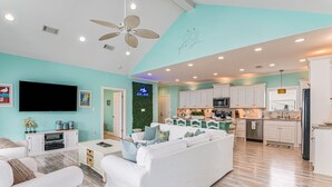 A modern living room with a white sofa, a flat-screen TV, and a ceiling fan. - Sweetheart savings! 3 min walk to Beach, Ocean View, WIFI, King 🛏 (Crystal Beach)