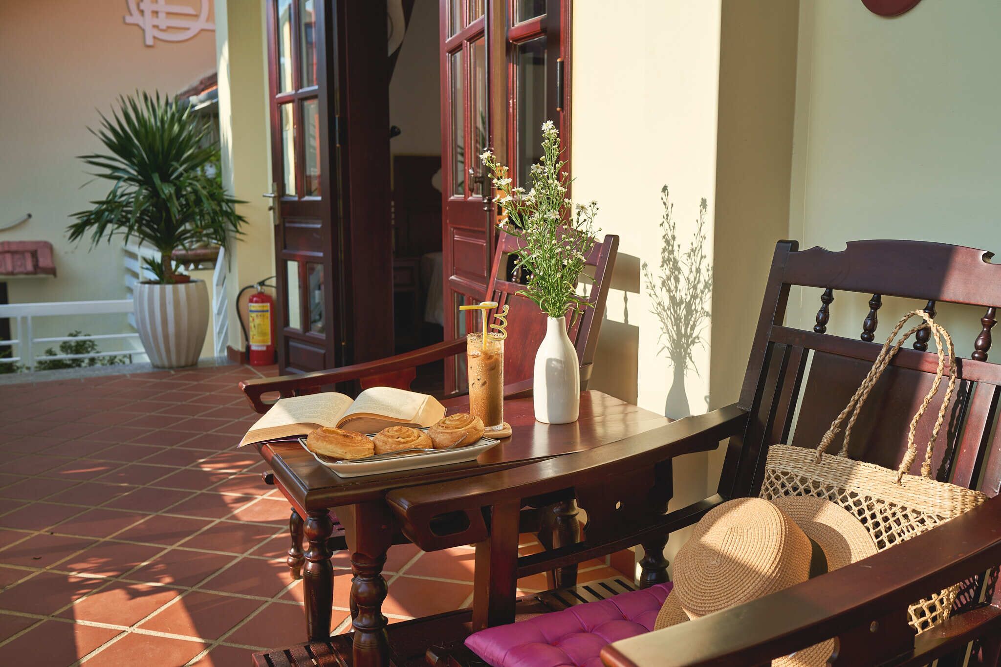 A wooden table with a tray of pastries, a bottle, and a vase with flowers.