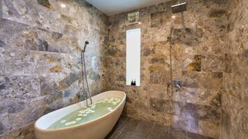 A bathroom with a freestanding bathtub, stone walls, and a shower area.