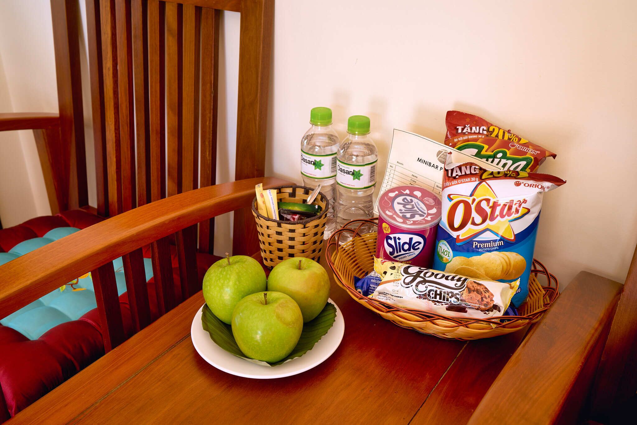 Een houten eettafel met een bord groene appels, een mand met lekkernijen en een fles water.