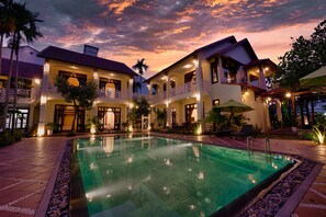 A hotel with a swimming pool, multiple balconies, and a sunset sky.
