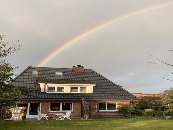 A house with a sloped roof, a chimney, and a visible rainbow in the sky.