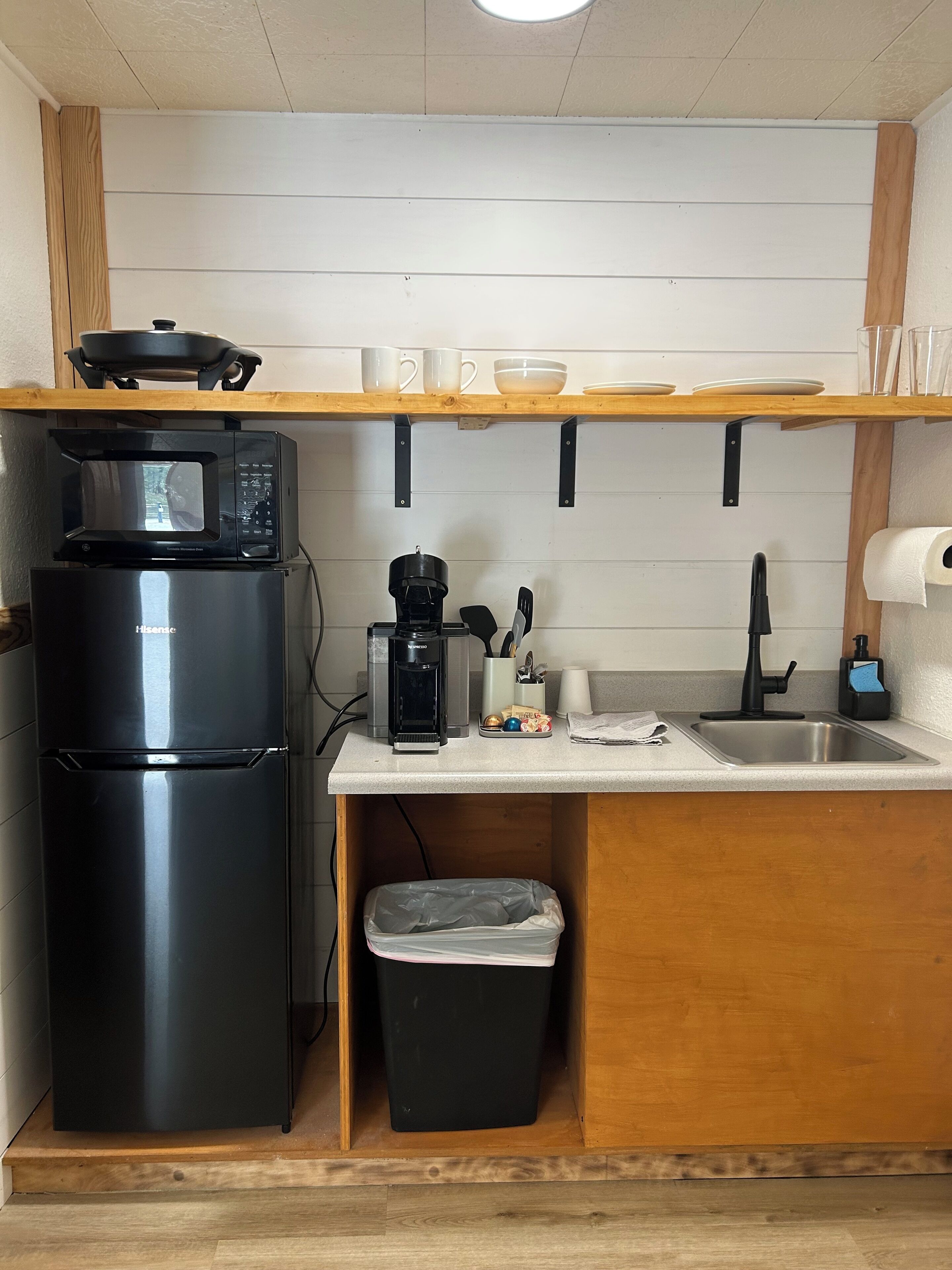 Una cocina compacta con un refrigerador negro, un microondas, una cafetera y un lavabo.