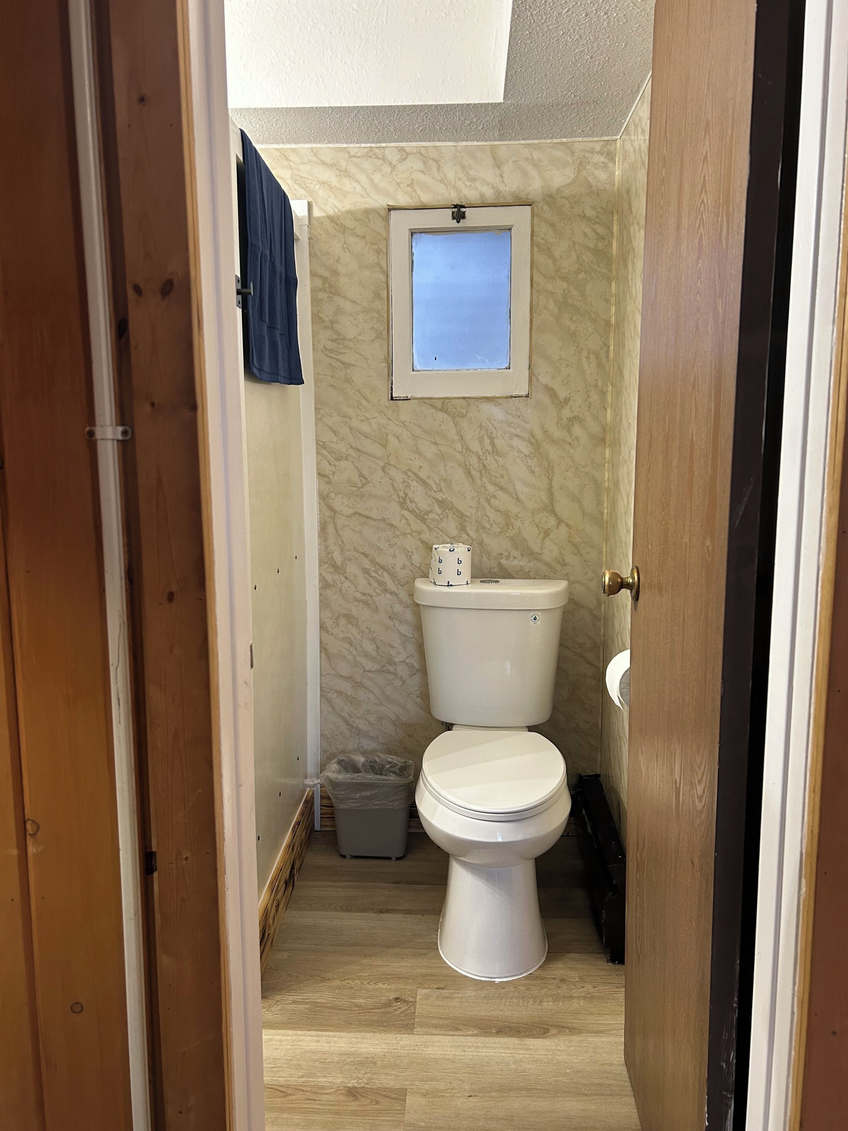 Een kleine badkamer met een toilet, een prullenbak en een raam.