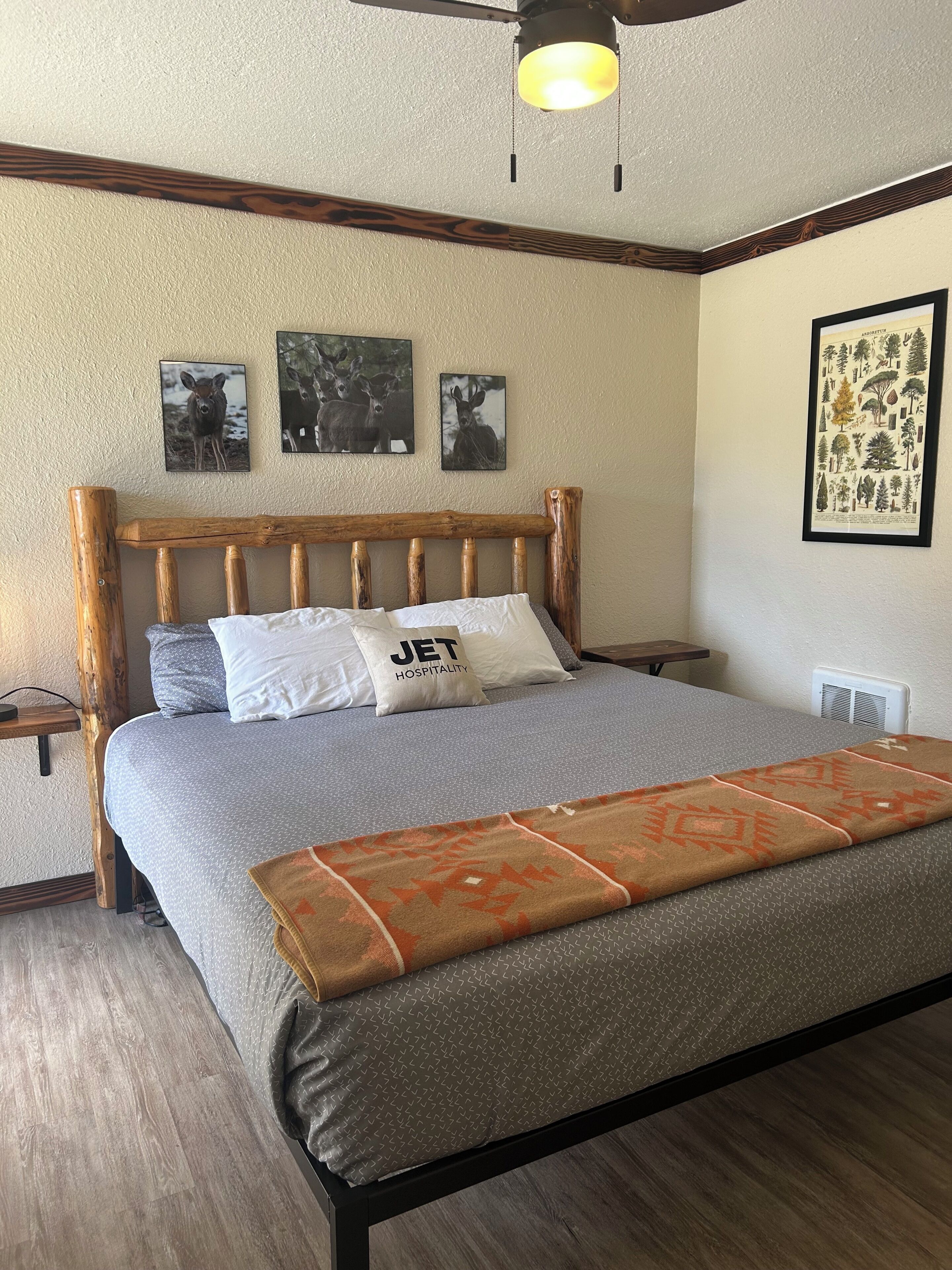 A bed with a wooden headboard, a gray bedspread, and a patterned throw blanket. There are three framed pictures on the wall above the bed.