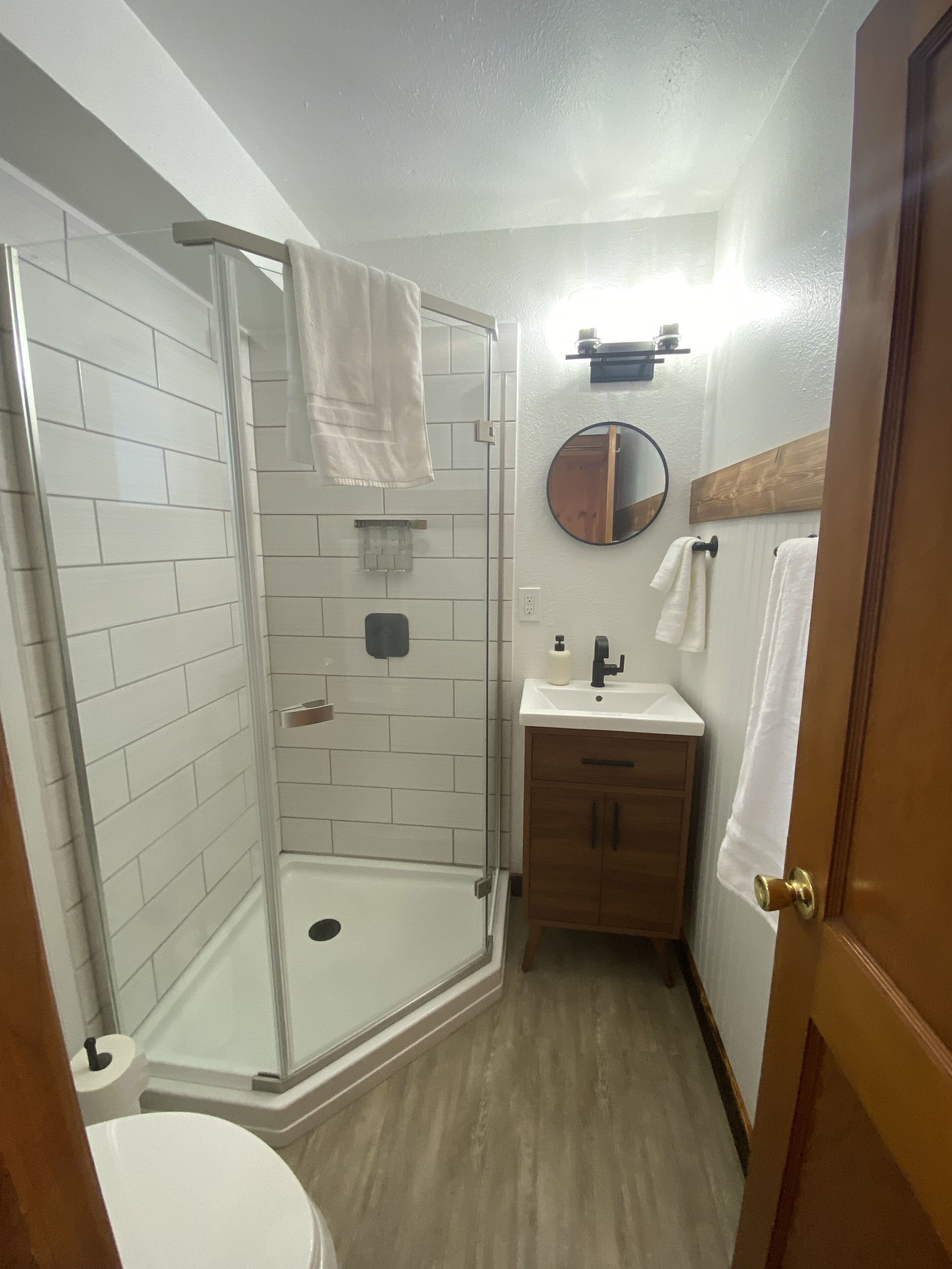 A bathroom with a glass shower enclosure, a sink, a mirror, and wooden cabinets.