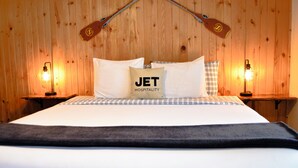 A hotel room with a wooden wall, a bed with white bedding, a pillow with "JET HOSPITALITY" text, and two bedside lamps. - Columbia Point Resort (Kettle Falls)