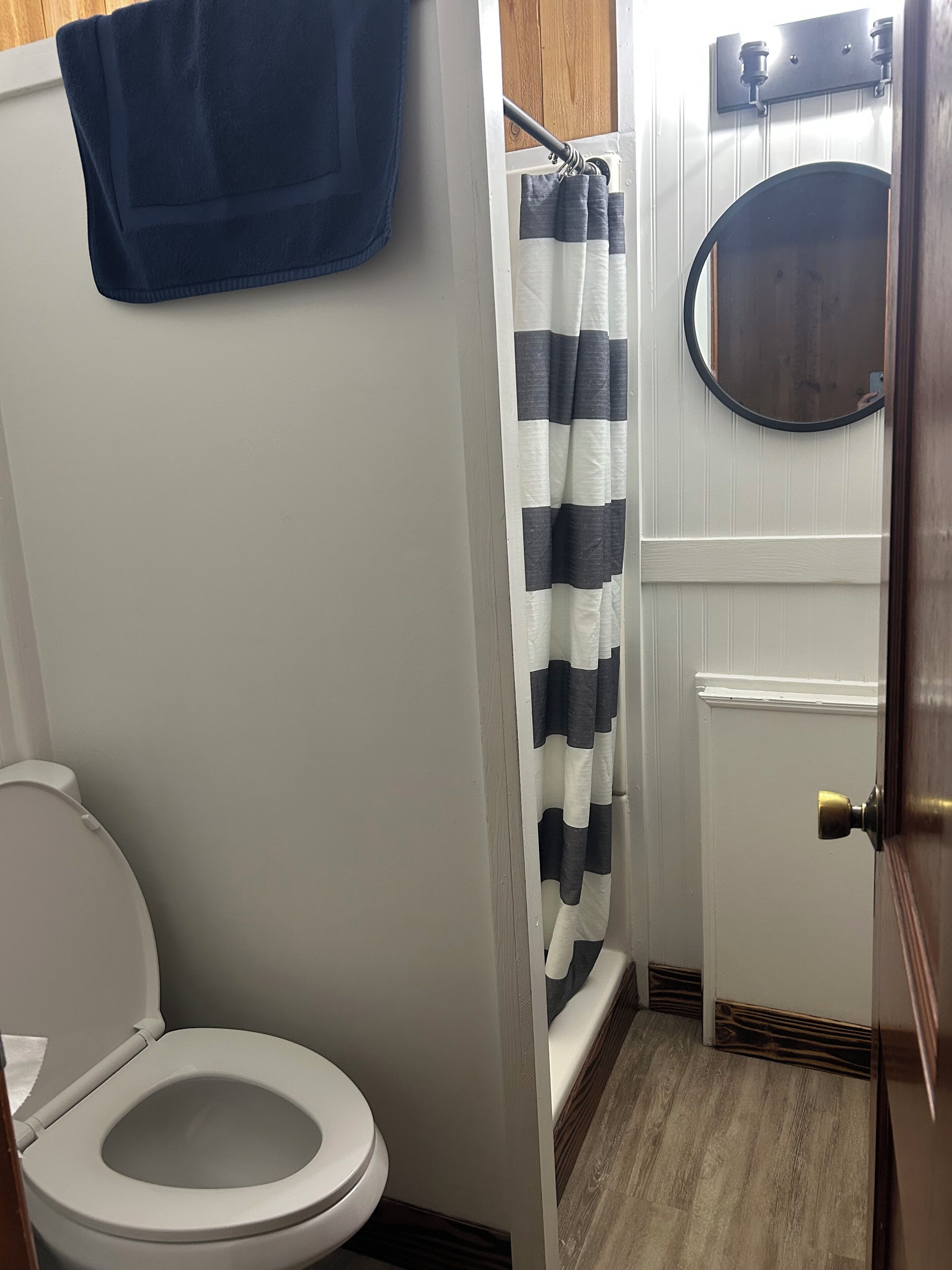 A bathroom with a toilet, a shower curtain, a mirror, and a towel hanging on the wall.
