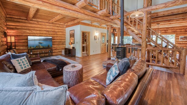 A spacious log cabin interior with a high ceiling, a fireplace, a large window, and a staircase leading to an upper level. - Tahoe Wanderer - Super Cool Luxury Log Cabin with NEW Kitchen, Private Hot Tub (Tahoe Vista)