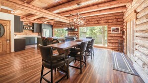 A rustic log cabin interior with a wooden dining table, chairs, a kitchen area, and large windows. - Tahoe Wanderer - Super Cool Luxury Log Cabin with NEW Kitchen, Private Hot Tub (Tahoe Vista)