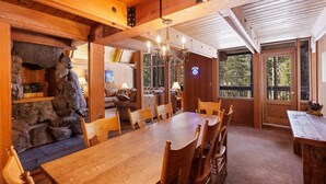 A wooden dining area with a large table and chairs, stone walls, and a cozy fireplace. - Snowy Paws Alpine Meadows - Ski Shuttle- Dog OK - Close to Slopes - Amazing Views (Olympic Valley)