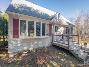 A single-story house with a covered porch, a small deck, and a front yard with mulch and trees.