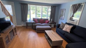 Una sala de estar con sofá, reposapiés, mesa de centro y mueble para televisión.