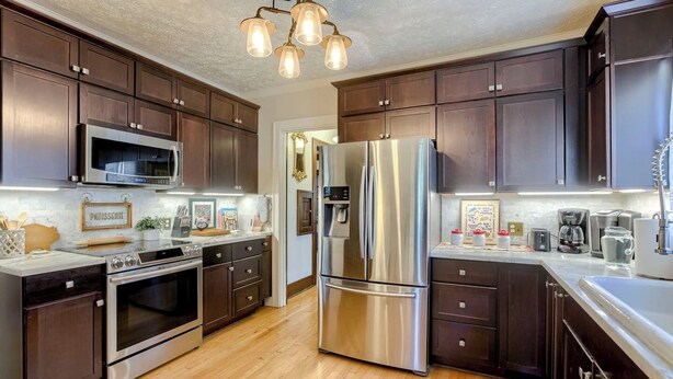 A modern kitchen with dark wood cabinets, stainless steel appliances, and a wooden floor.