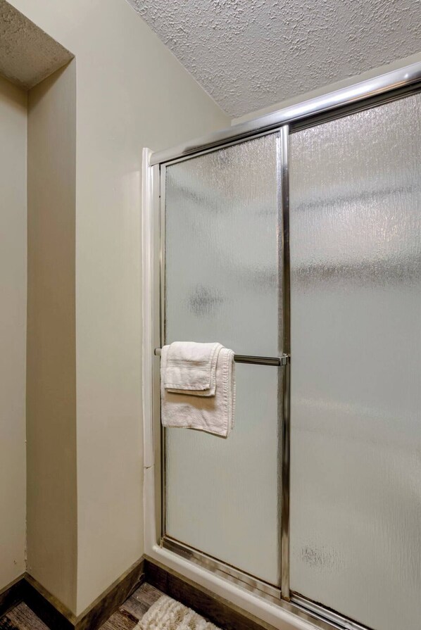 Une salle de bain avec une porte de douche en verre, une serviette blanche accrochée à la porte et un plancher en bois.