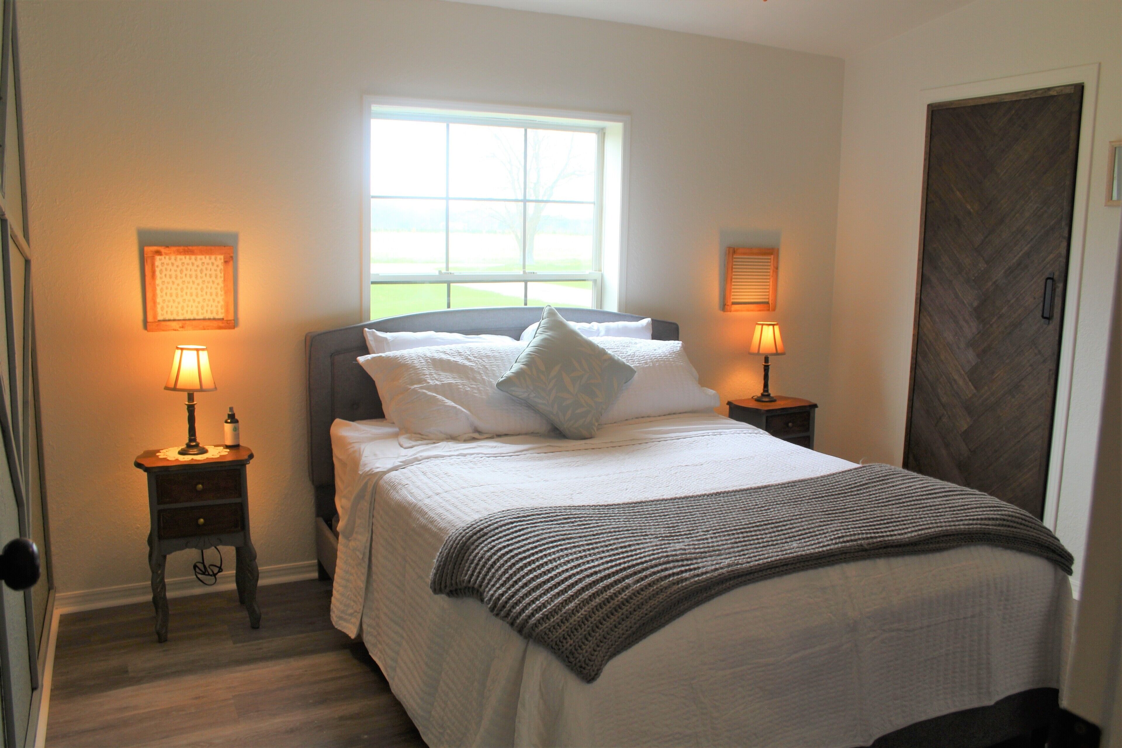 A bedroom with a bed, two bedside lamps, a window, and a door.