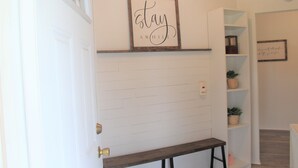 A hallway with a white brick wall, a wooden bench, and a shelf with a framed sign that reads "stay awhile". - Edward House, on 7 acres, not far from Notre Dame & Golf Course (Walkerton)
