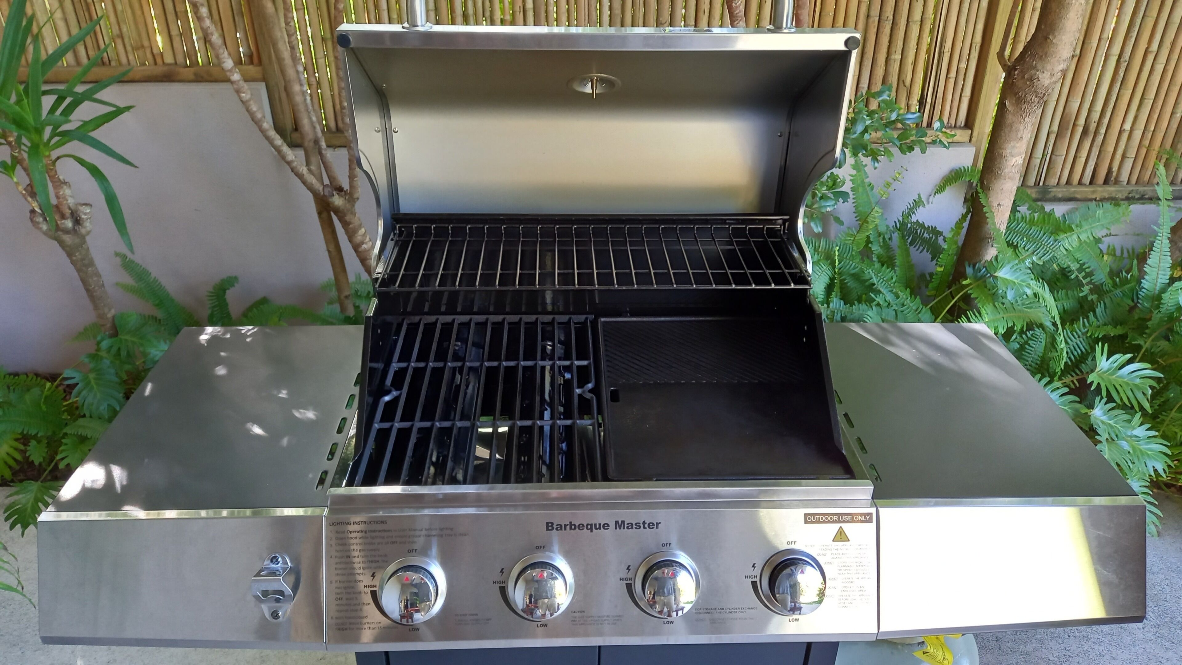 Ruostumattomasta teräksestä valmistettu grilli, jonka kylkeen on painettu teksti ”Barbeque Master”. Grillissä on neljä säätönuppia ja ilmastointiaukollinen kansi.