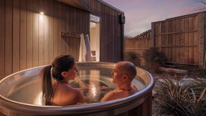 A couple in a hot tub outside a wooden house with a wooden fence in the background. - Central Queenstown Villa & Spa (Queenstown)