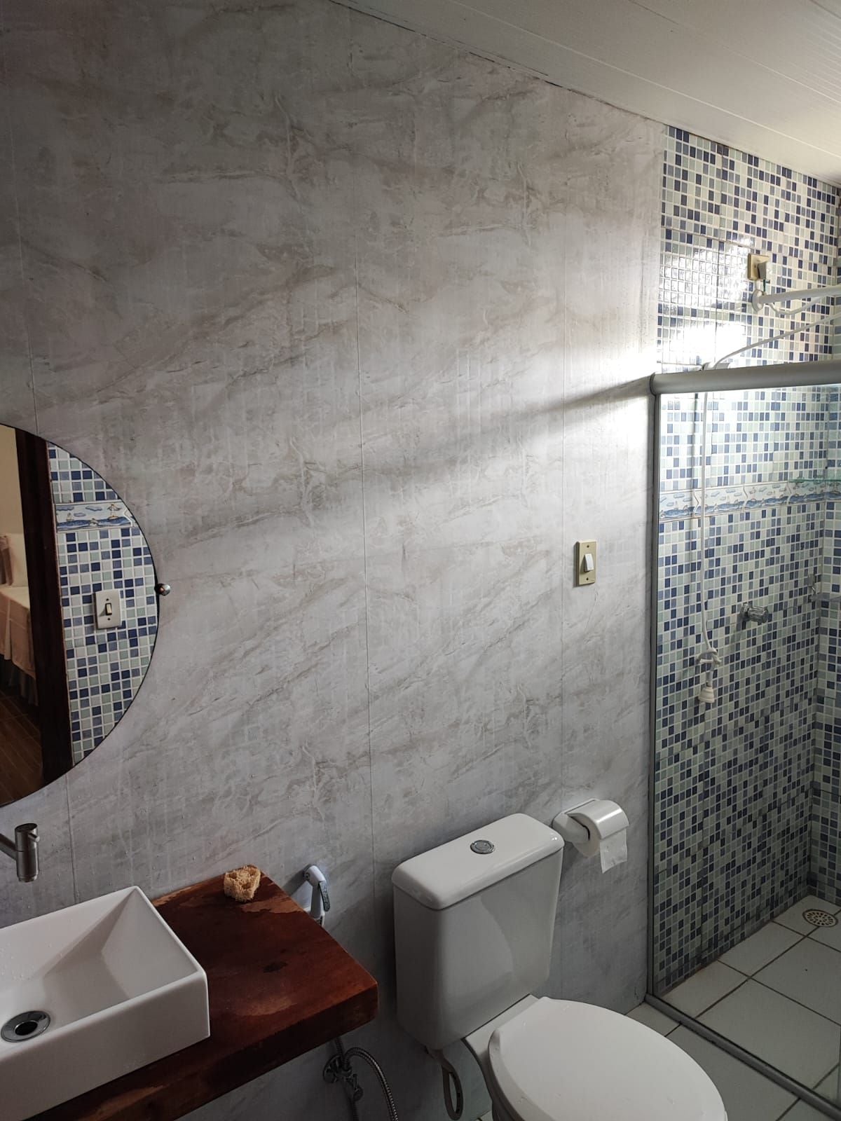 Et badeværelse med en marmorvæg, en vask med træbordplade, et toilet og en bruseniche med mosaikfliser.