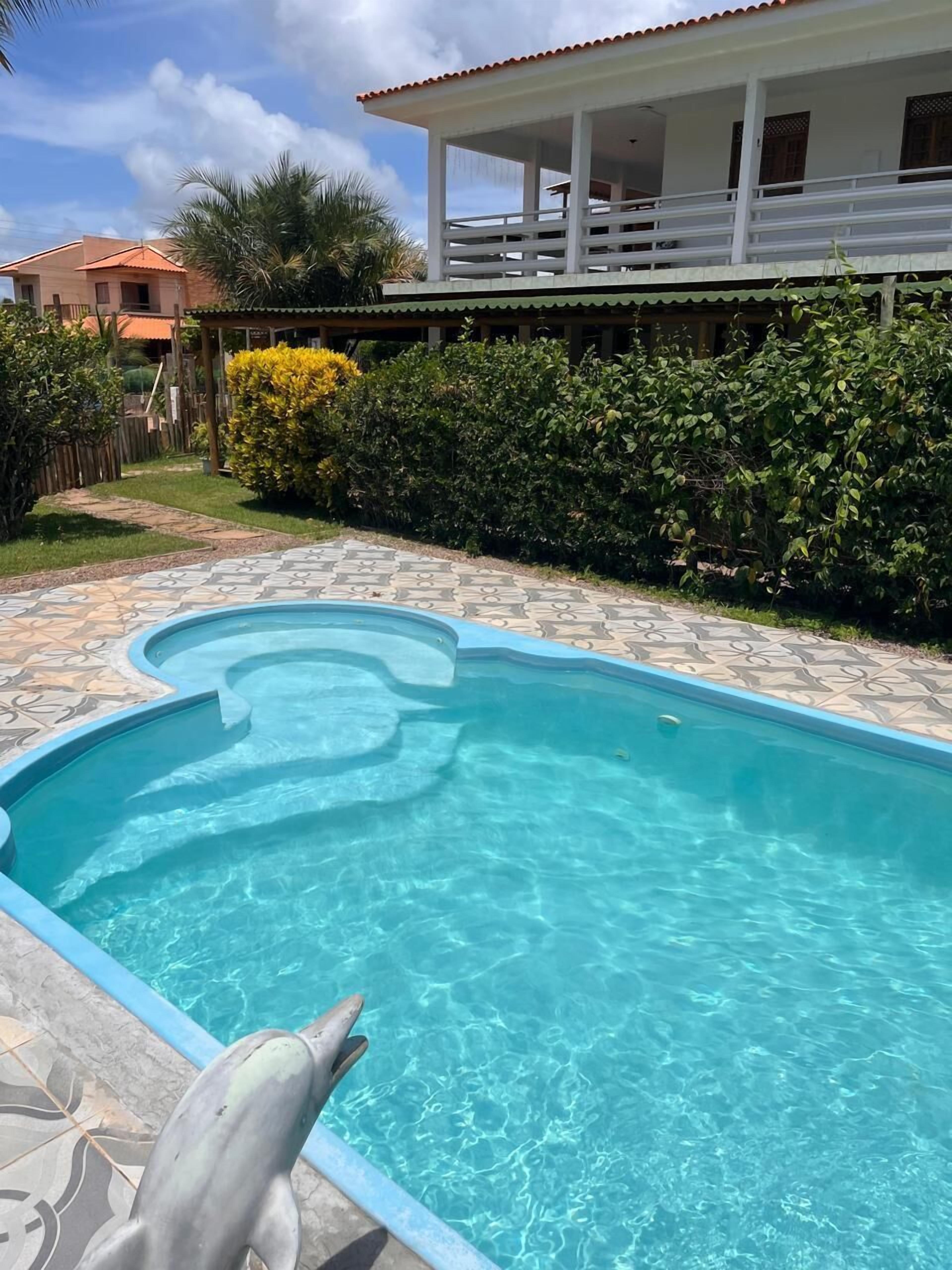 Una piscina con una estatua de delfín, rodeada por un patio empedrado y una casa con balcón.