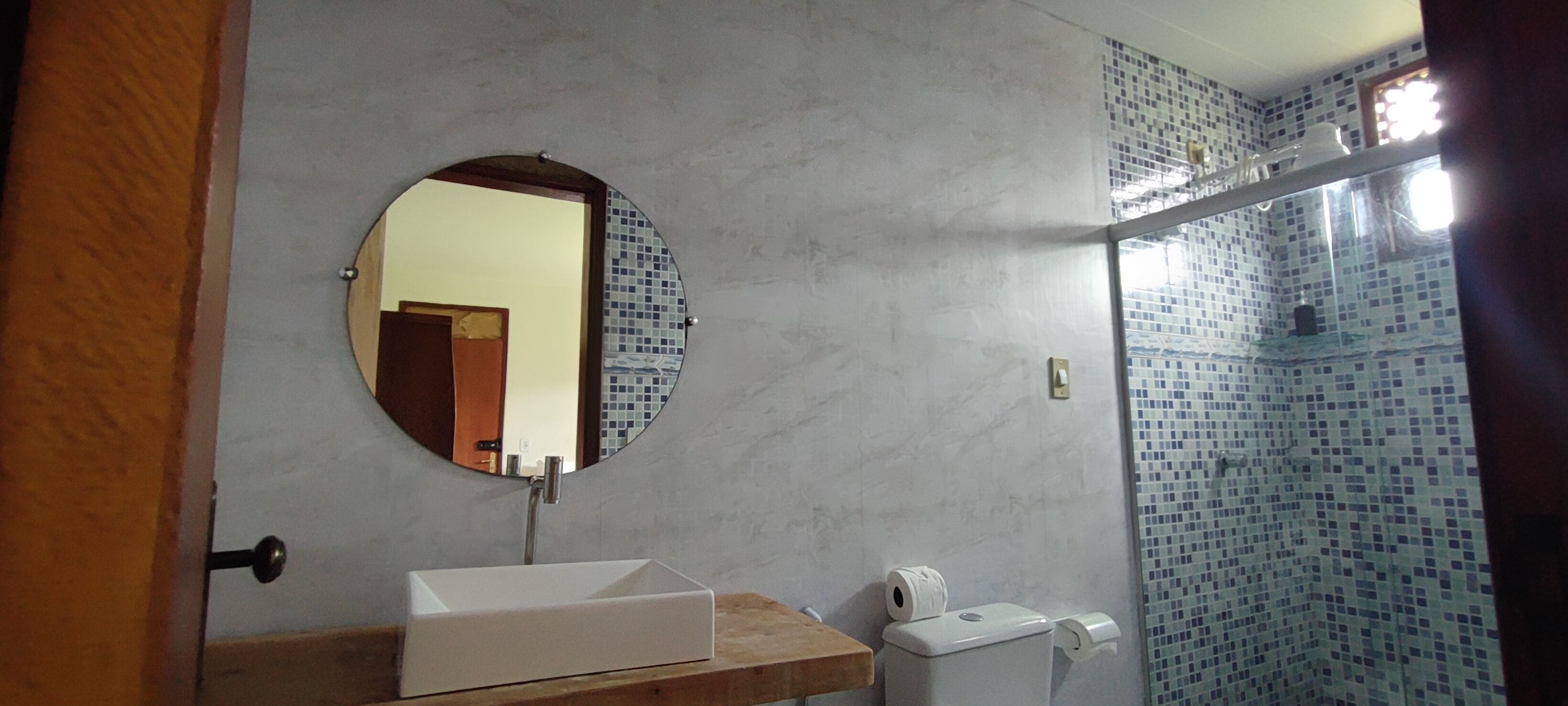 Une salle de bain avec un lavabo rectangulaire, un miroir rond et des toilettes.