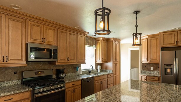 A kitchen with wooden cabinets, granite countertops, a stainless steel refrigerator, a microwave, a stove, and pendant lighting. - 4BR/3BA on a Golf Course close to Beach, Casinos & Downtown Ocean Springs! (Ocean Springs)
