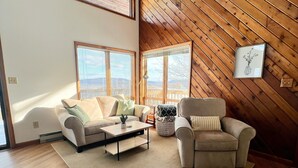 A modern living room with a wooden sloped ceiling, two sofas, a coffee table, and a large window.