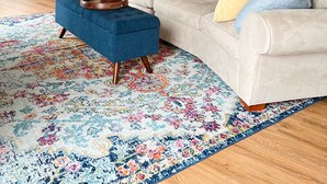 A modern living room with a large beige sectional sofa, a blue ottoman, and a colorful patterned rug.