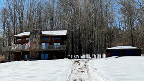 A cabin with a stone foundation and wooden exterior, surrounded by a snow-covered landscape and leafless trees.