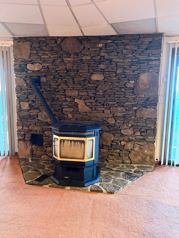 En stenmur med en vedeldad kamin i ett rum med heltäckningsmatta på golvet och ett tak med infälld belysning.