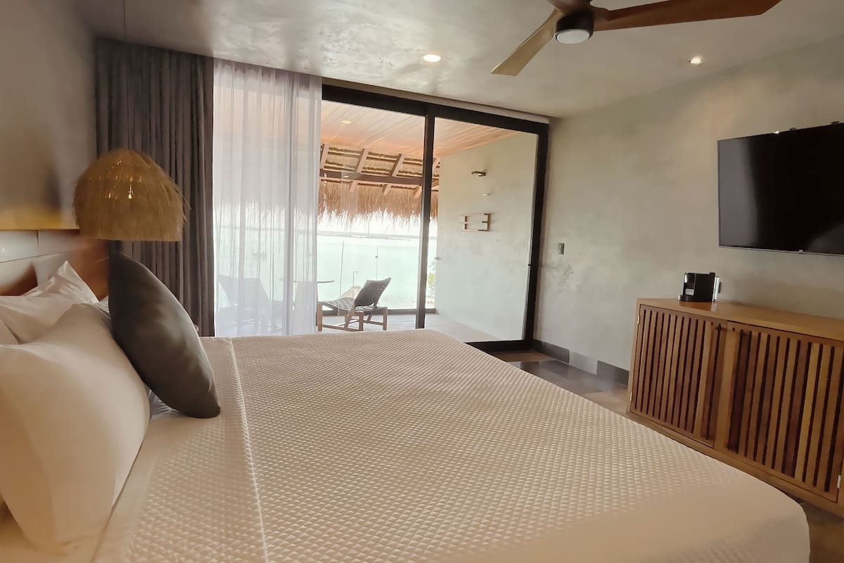Una habitación de hotel moderna con una cama grande, un televisor, un armario de madera y un balcón con vistas.