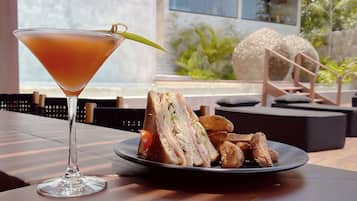 Un verre à martini, agrémenté d’une garniture, est posé sur une table où se trouvent une assiette de nourriture et des plats frits.