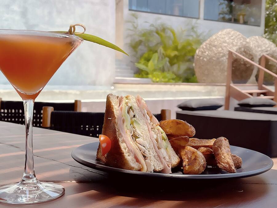 Un verre à martini, agrémenté d’une garniture, est posé sur une table où se trouvent une assiette de nourriture et des plats frits.