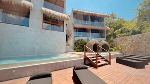 Un moderno resort con piscina, terraza de madera y edificios con techo de paja.