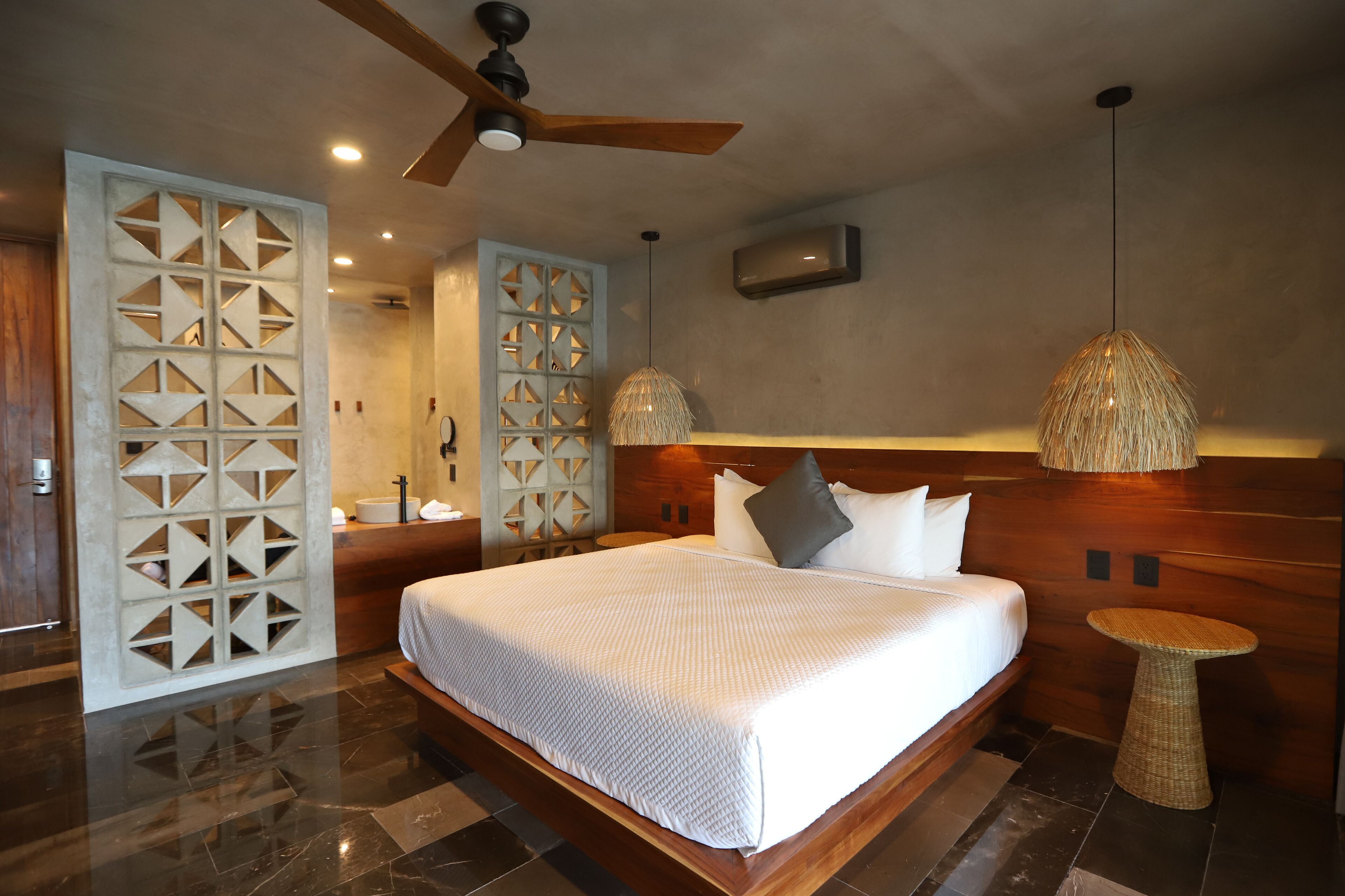 A modern hotel room with a large bed, wooden headboard, a ceiling fan, and a small round table.