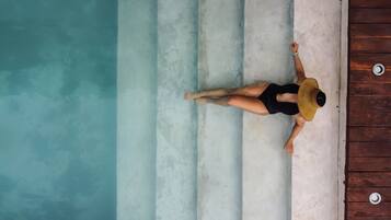 Una persona recostada en una cubierta de madera junto a una piscina con agua azul cristalina.