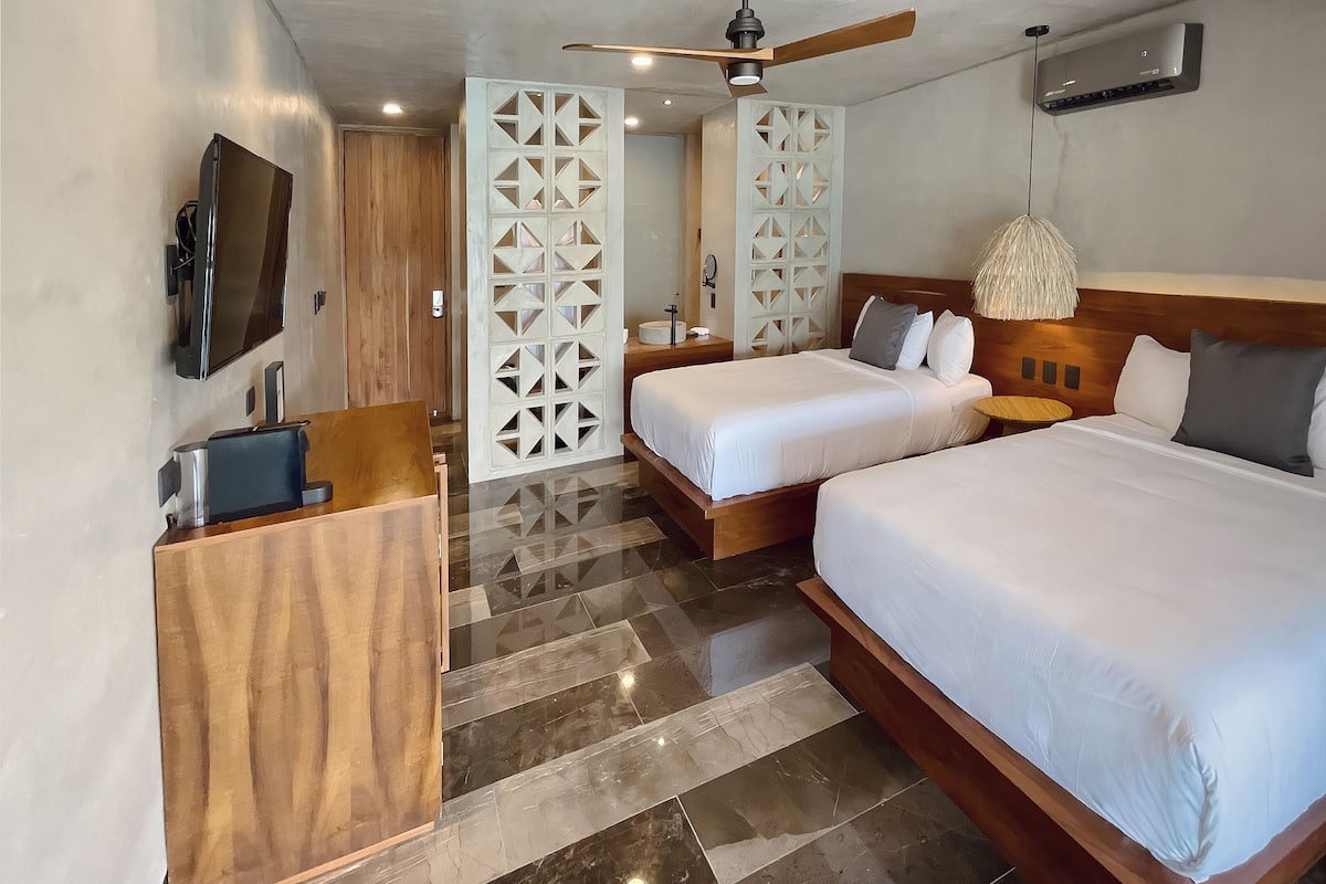 Habitación de hotel con dos camas, televisor, escritorio de madera y ventilador de techo moderno.