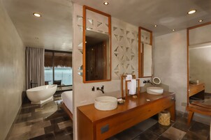 Un baño moderno con una bañera independiente, un tocador de madera con un lavabo redondo y un espejo grande.