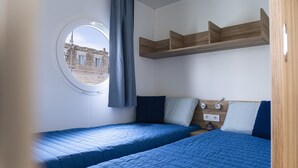 Een kamer met twee bedden, een raam met uitzicht op gebouwen, en een houten plank boven de bedden.