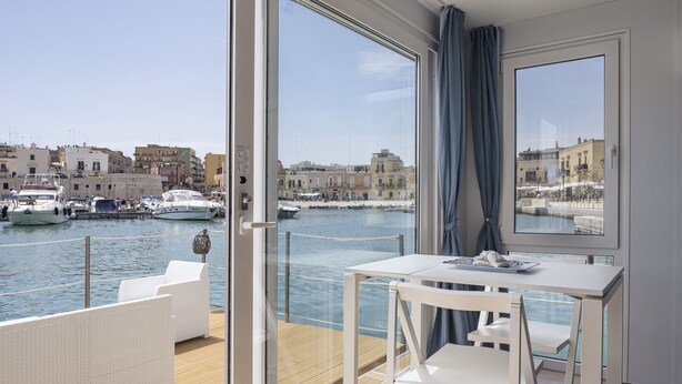 Een balkon met een tafel en stoelen, uitzicht op een jachthaven met boten en gebouwen op de achtergrond.
