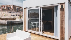 Een modern gebouw met een glazen deur die uitkomt op een terras met witte rieten meubels.