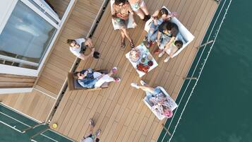 A deck with people relaxing, a table with food, and a view of the water.