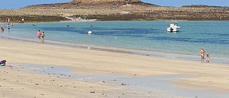 A beach with a rocky hill in the background, a boat in the water, and people on the shore.