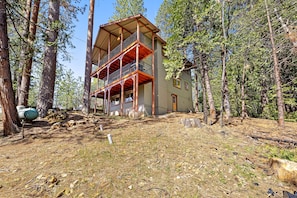 A two-story wooden cabin with a balcony, surrounded by a forest.