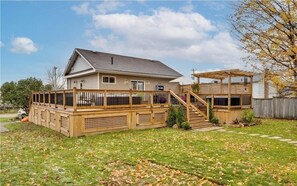 Enjoy the expansive deck with a staircase leading to an upper level, surrounded by a well-manicured lawn and a tree with vibrant foliage.
