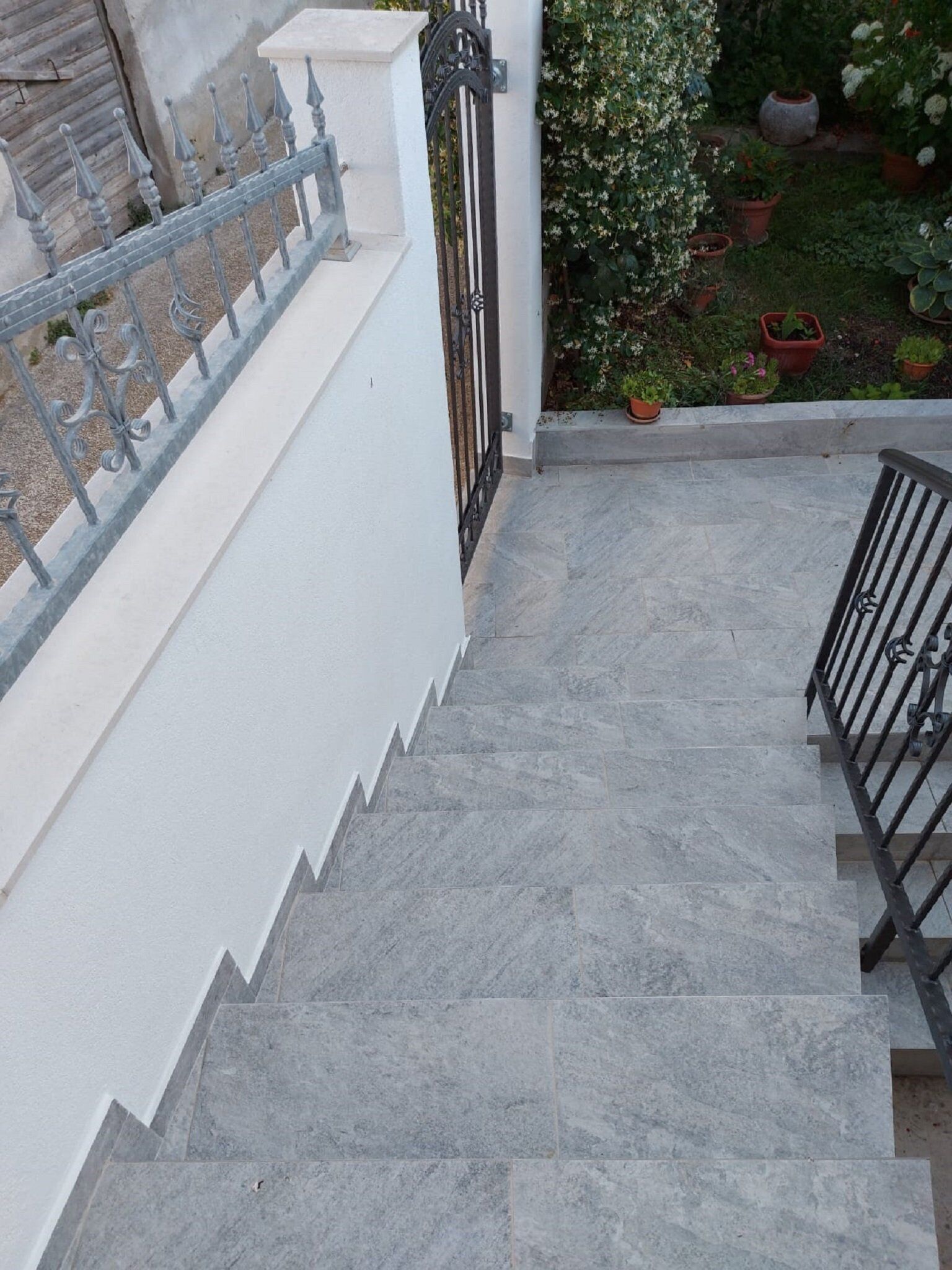 A staircase with grey stone steps leading to a white wall with a black metal railing.