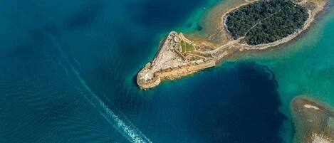 An aerial view of a coastal area with a marina, a small island with a fort, and surrounding greenery.