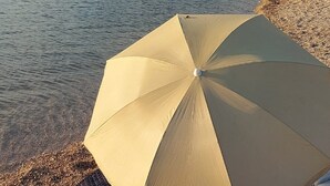 Una playa con un bote amarrado, gente nadando y una tienda de campaña con paraguas.