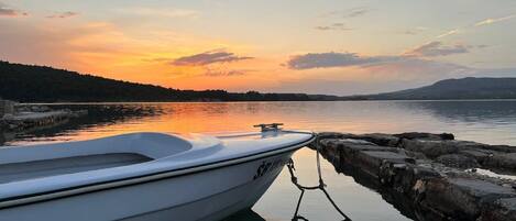 A boat tied to a dock with a calm lake and a sunset in the background.
